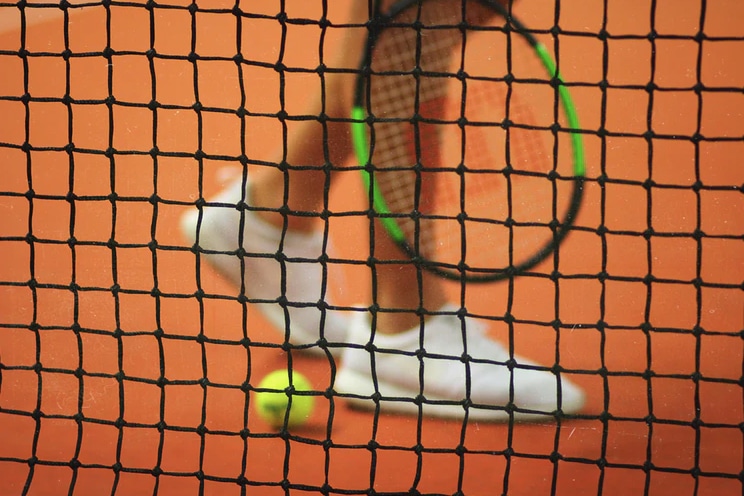 Tennis net with a tennis player, racket, and ball on a clay courth