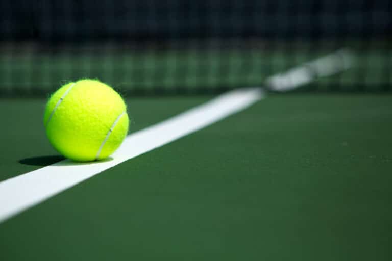 Tennis ball sitting on line of tennis court