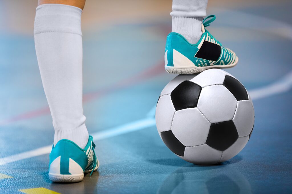close-up of feet, one on ball, of person playing futsal on indoor court